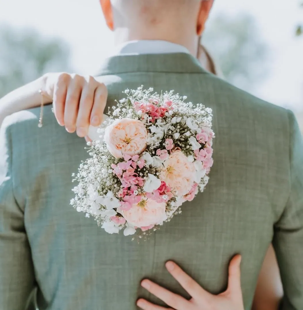 Bruid houdt een boeket met roze rozen en gipskruid tegen de rug van de bruidegom