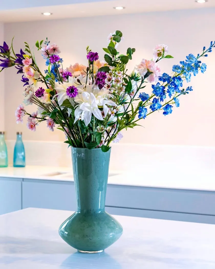 Zijden veldbloemen in een turquoise vaas op een keukeneiland